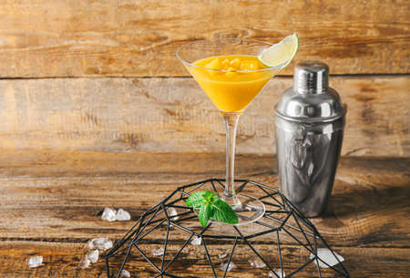 Glass of tasty mango margarita and shaker on wooden backgroundの写真素材