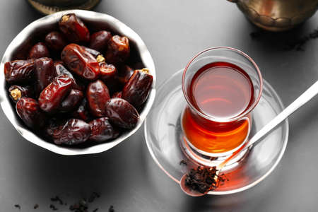 Glass of tasty Turkish tea and bowl with dates on dark backgroundの写真素材