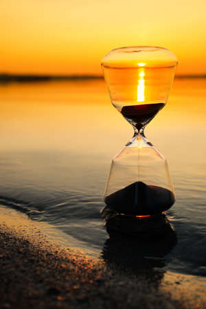 Stylish hourglass near river at sunset