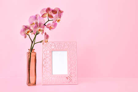 Vase with beautiful orchid flowers and blank photo frame on color backgroundの写真素材
