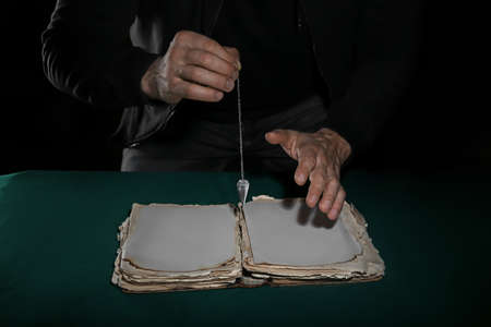 Fortune teller with spell book and pendulum on dark backgroundの写真素材