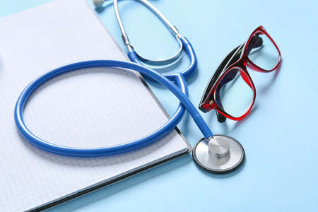Modern stethoscope, notebook and eyeglasses on color background, closeupの写真素材