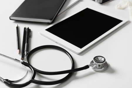 Composition with modern stethoscope and tablet computer on light background, closeup