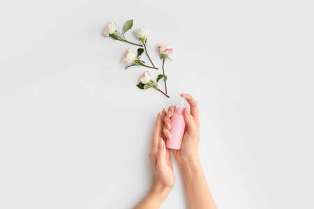 Female hands with cream and beautiful flowers on light backgroundの写真素材