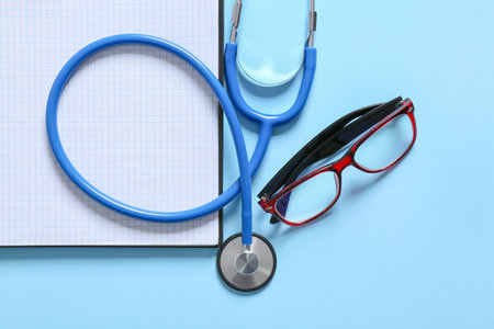 Composition with modern stethoscope, notebook and eyeglasses on color background, closeupの写真素材