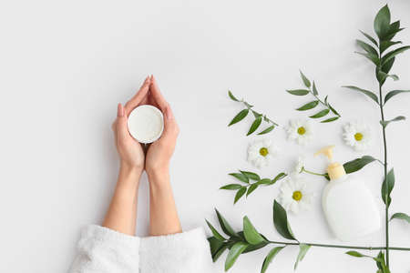Female hands with cream, leaves and beautiful flowers on light backgroundの写真素材