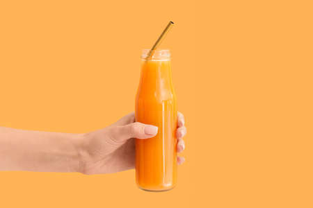 Female hand with bottle of tasty smoothie on color backgroundの写真素材