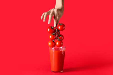 Female hand with glass of tasty tomato smoothie on color backgroundの写真素材