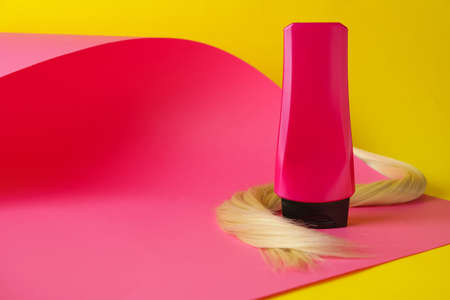 Bottle of hair shampoo and strand on color backgroundの写真素材