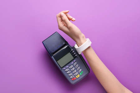 Female hand with smart watch and payment terminal on color backgroundの写真素材