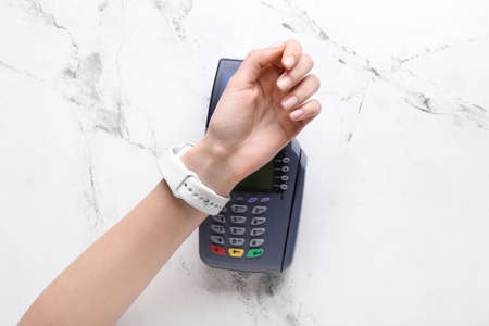 Female hand with smart watch and payment terminal on light backgroundの写真素材