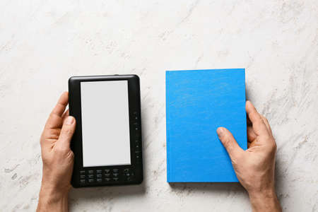 Male hands with e-reader and book on light backgroundの写真素材
