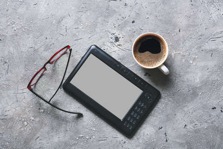 E-reader, eyeglasses and cup of coffee on gray backgroundの写真素材