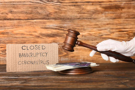 Judge with gavel, money, credit cards and paper sheet with text CLOSED BANKRUPTCY CORONAVIRUS on wooden backgroundの写真素材