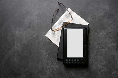 E-reader, notebook, newspaper and eyeglasses on dark backgroundの写真素材