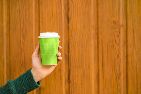 Woman with takeaway cup of tasty latte near wooden wallの写真素材