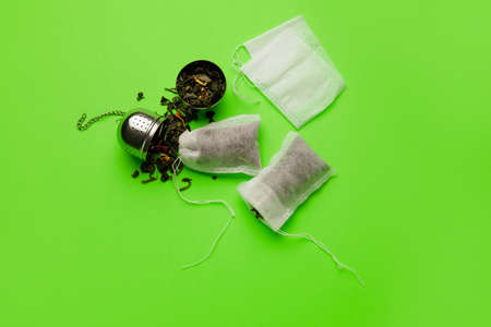 Tea bags and strainer with dry leaves on color background