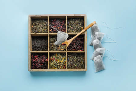 Tea bags and box with dry leaves on color background