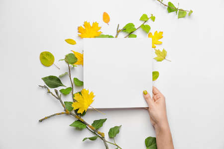 Female hand with blank card and autumn leaves on white backgroundの写真素材