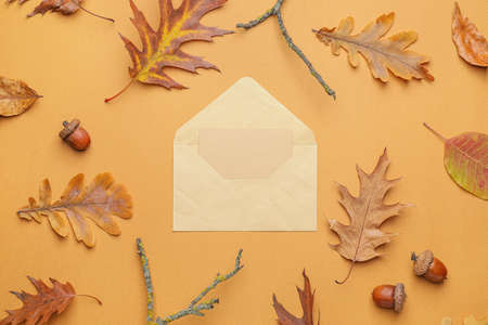 Envelope with blank card and autumn leaves on color backgroundの写真素材