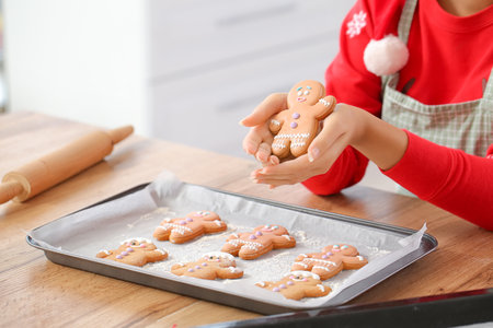 Young woman with tasty homemade gingerbread cookies in kitchen on Christmas eve