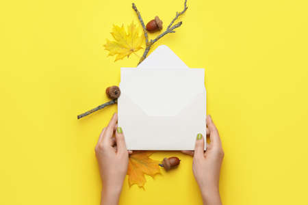 Female hands with envelope, blank card, acorns and autumn leaves on color backgroundの写真素材