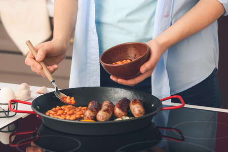 Woman cooking traditional English breakfast on electric stove in kitchenの写真素材