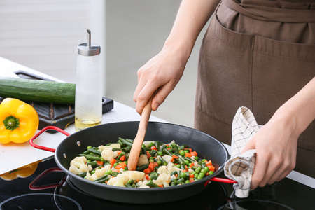 Woman cooking vegetables on electric stove in kitchenの写真素材