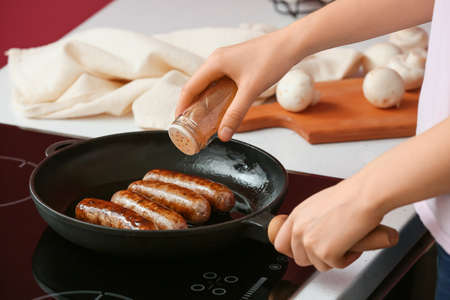 Woman cooking sausages on electric stove in kitchenの写真素材