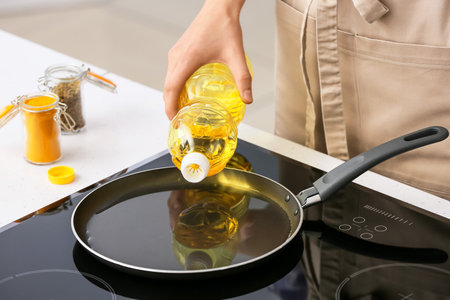 Woman pouring sunflower oil onto frying pan in kitchenの写真素材