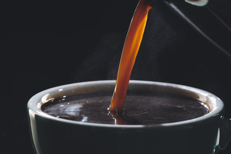 Pouring of hot coffee in cup on dark background, closeupの写真素材