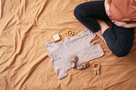 Pregnant woman with baby clothes and toys on bedの写真素材