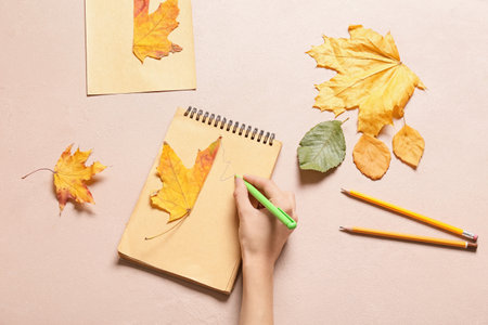 Woman drawing autumn leaf in notebook on color backgroundの写真素材