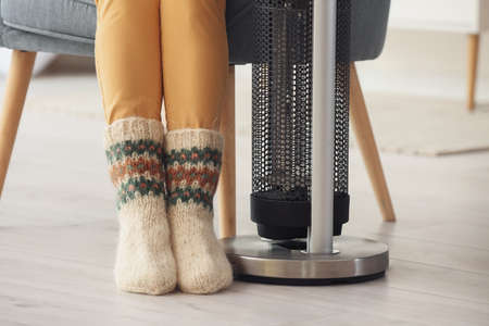 Mature woman near electric heater at home. Concept of heating seasonの写真素材