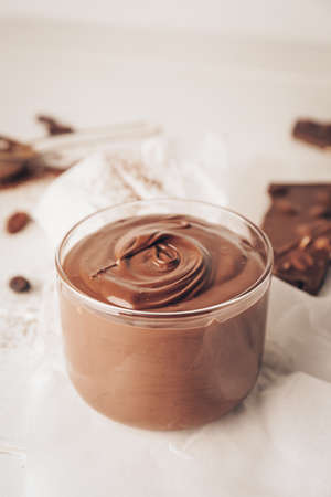 Glass bowl of tasty melted chocolate on light wooden background