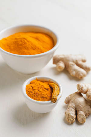 Bowls with turmeric powder and roots on white wooden backgroundの写真素材