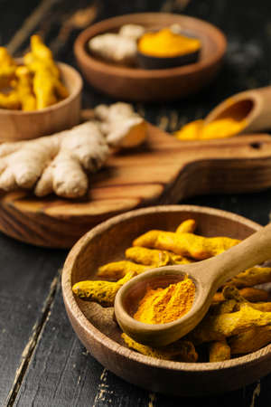 Bowl with turmeric powder and roots on dark wooden backgroundの写真素材