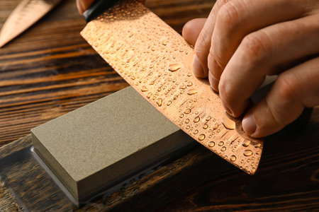 Man sharpening knife on wooden background, closeupの写真素材