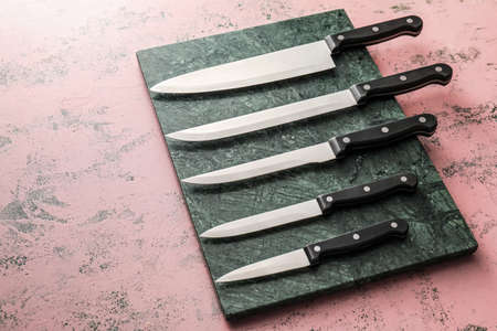 Board with set of knives on color background