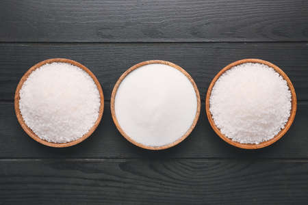 Bowls with different salt on dark wooden background