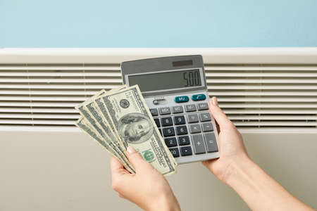 Woman with calculator and money near radiator. Concept of heating seasonの写真素材