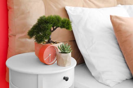 Bedside table with alarm clock and houseplants near bed, closeupの写真素材
