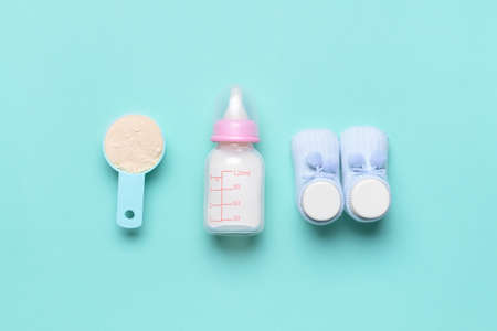 Bottle of baby milk formula and booties on color background