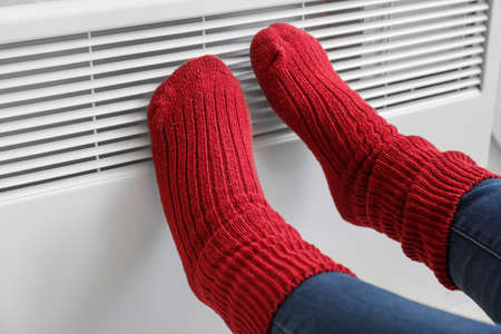 Woman warming feet at radiator. Concept of heating seasonの写真素材