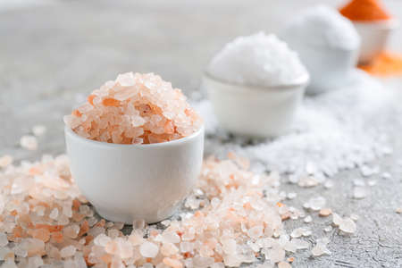Bowls with different salt on gray background, closeup