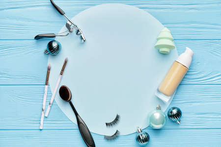 Christmas composition with cosmetics and blank card on color wooden background