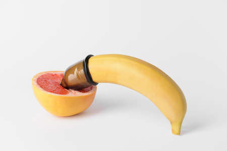 Banana in condom and grapefruit on white background. Erotic conceptの写真素材