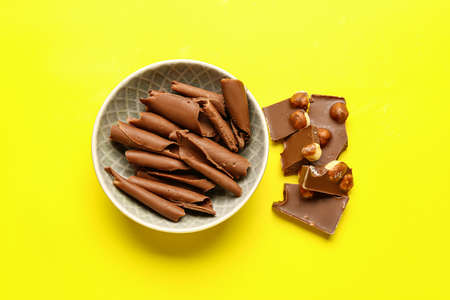 Bowl with curls and pieces of chocolate on color background