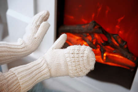 Young woman sitting near electric fireplace at home. Concept of heating seasonの写真素材