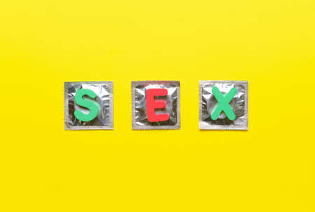 Word SEX with condoms on color background